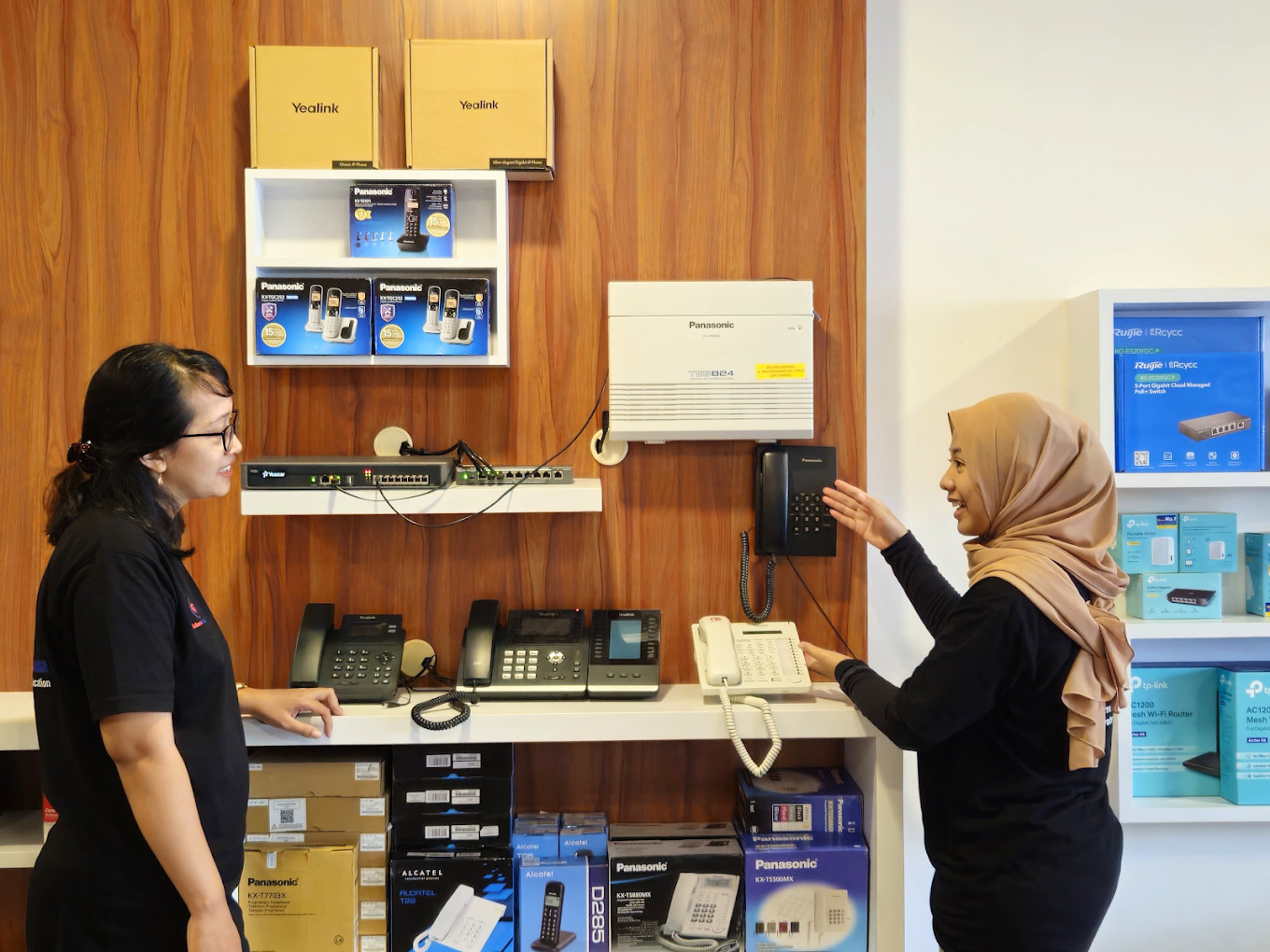 Two staff members beside a display of Panasonic and Yealink PABX phones