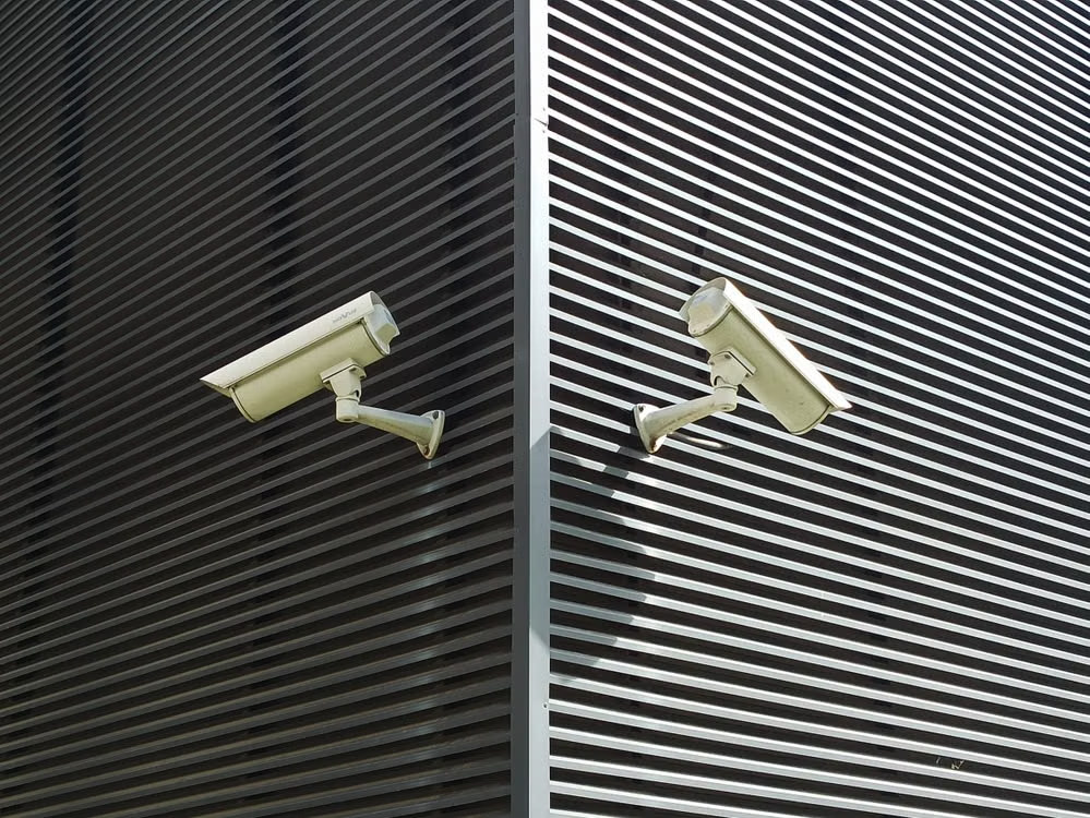 Two bullet CCTV cameras mounted on a dark slatted facade
