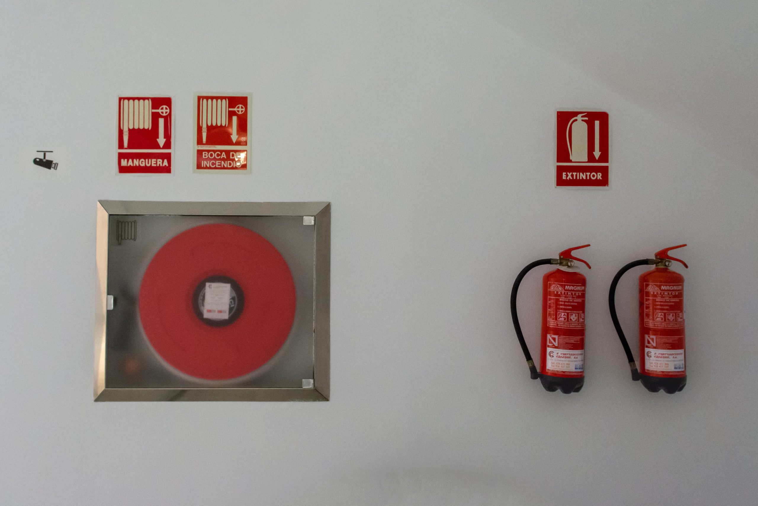 Fire hose reel cabinet, safety signs and two fire extinguishers on a white wall