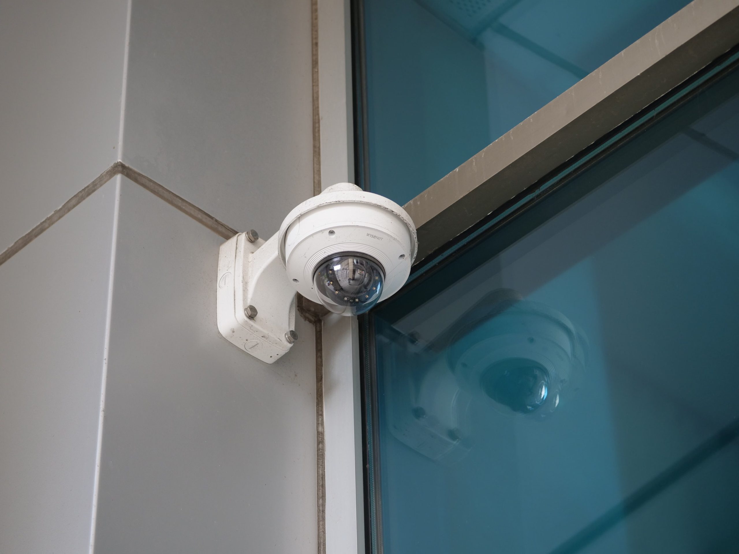 Dome CCTV camera mounted on a wall bracket beside a glass window